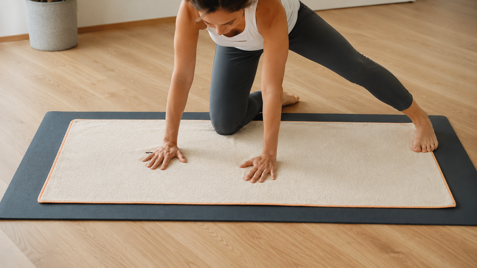 Yoga practitioner applying hand and foot pressure to a full-length towel positioned over a yoga mat